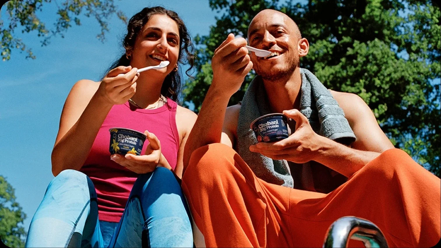 Two people eating Chobani yogurt outside.