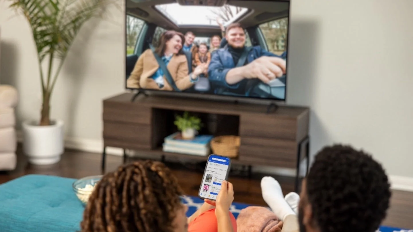 A couple at home watching tv while shopping on a mobile phone.