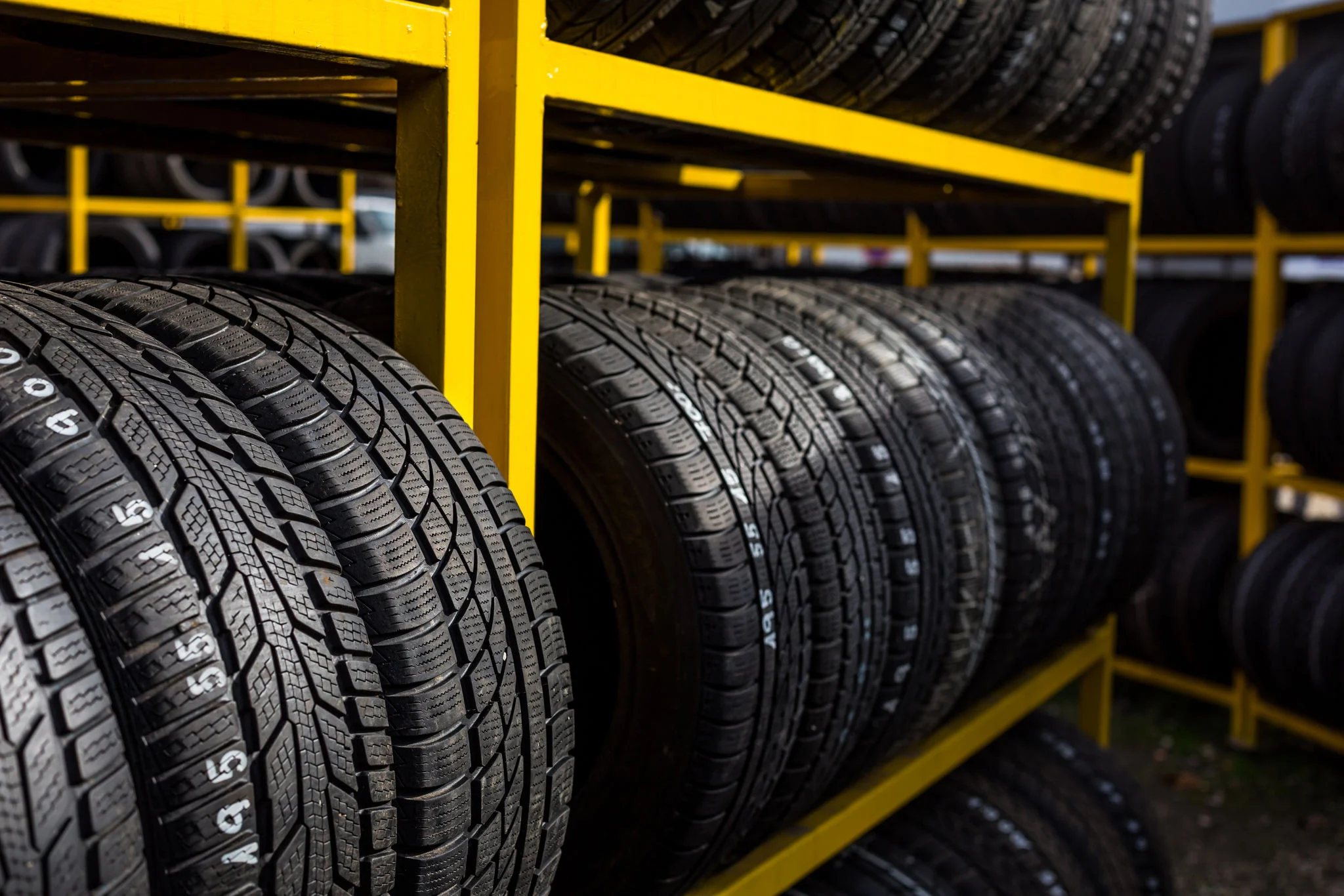 Rows of new car tires neatly arranged on yellow racks in an automotive store.