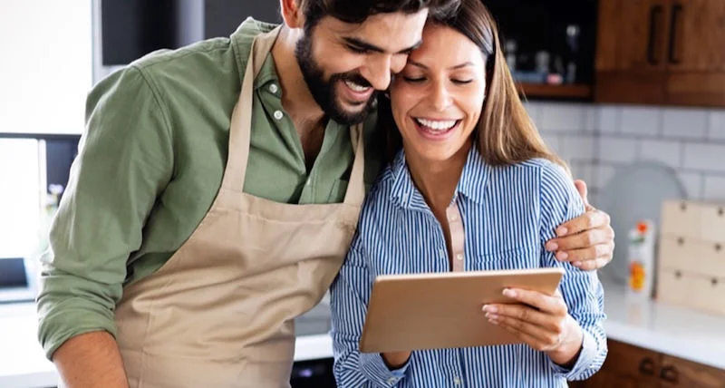 A couple in the kitchen looking at a tablet device.