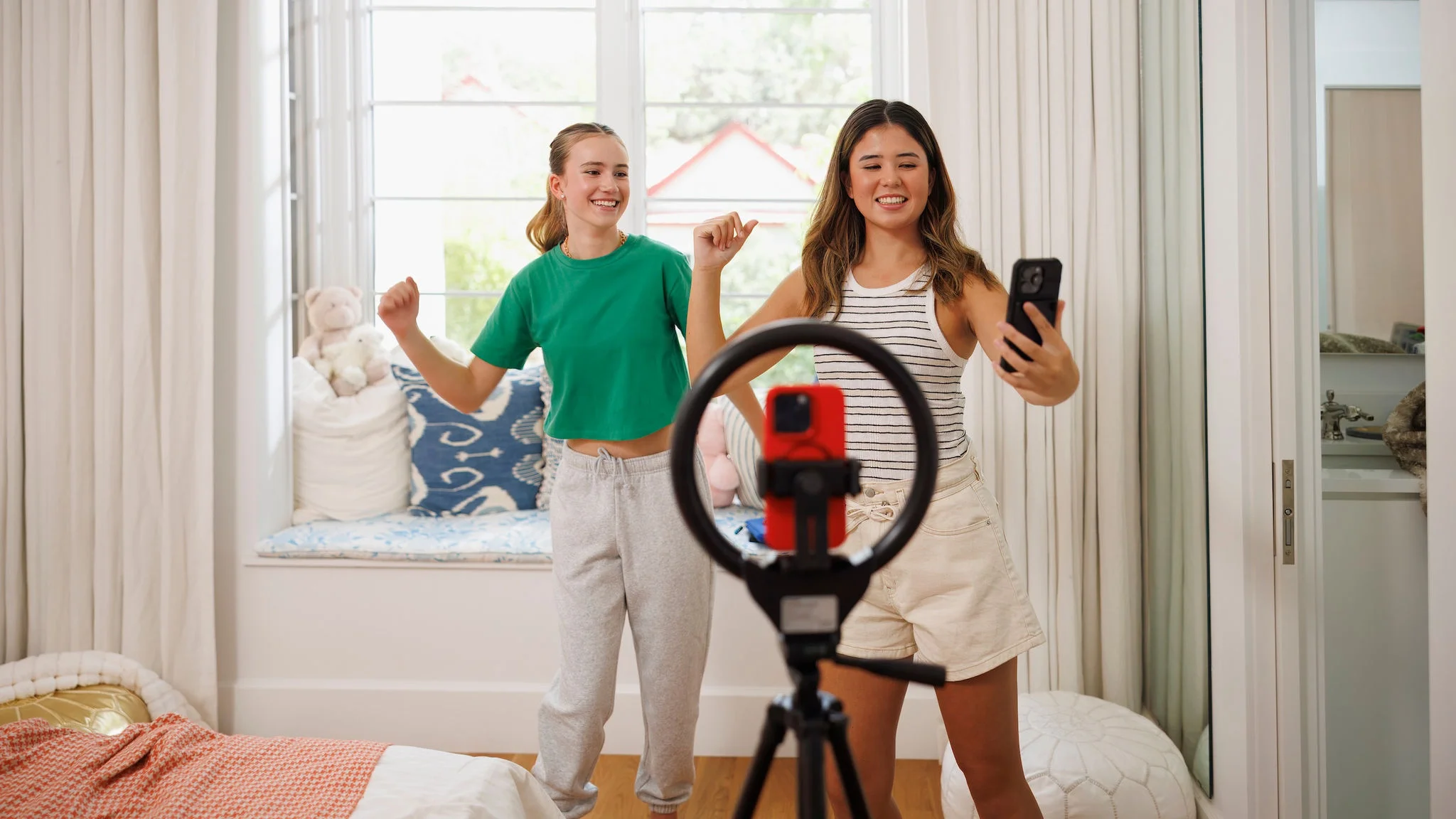 Two female friends using mobile phones to record themselves dancing.