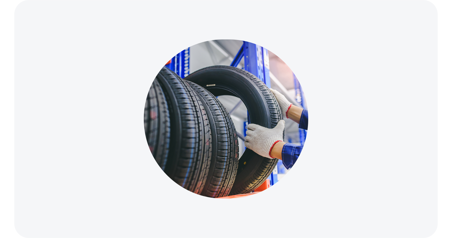 Gloved hands placing a new tire on a blue metal rack in an automotive service area.