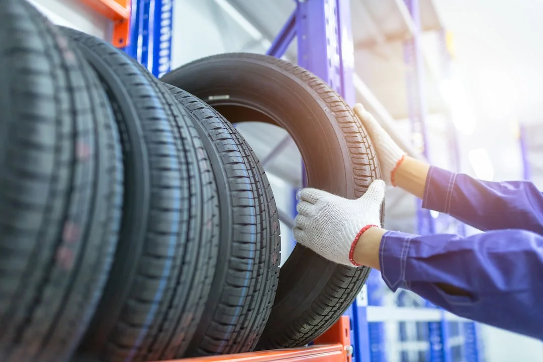 Mechanic picking a car tire from shelf in tire shop.