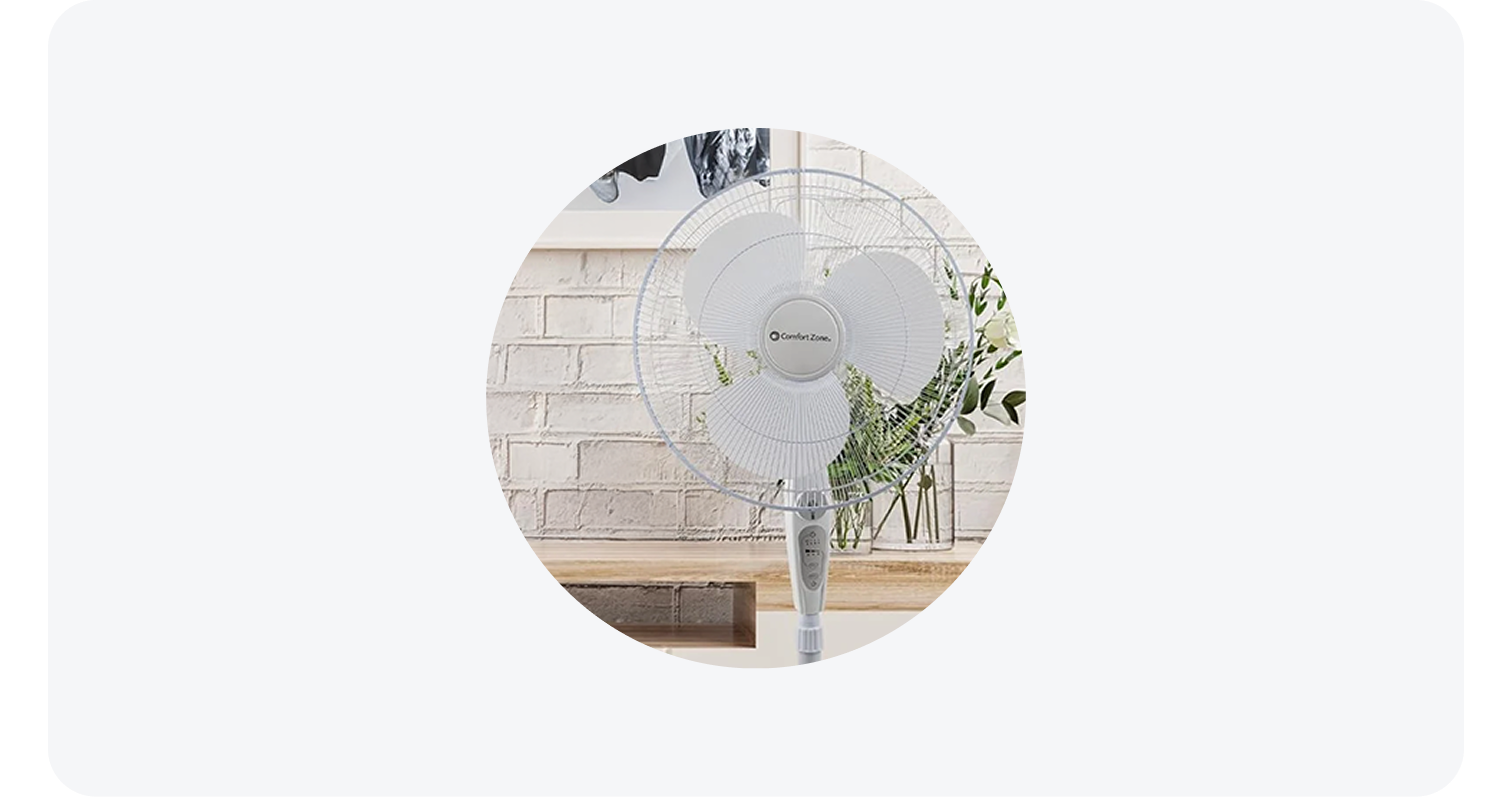 Comfort Zone white oscillating fan in a home setting in front of a brick wall and flowers.