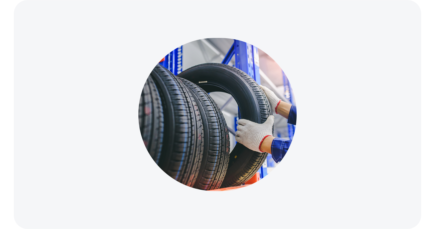 Gloved hands placing a new tire on a blue metal rack in an automotive service area.